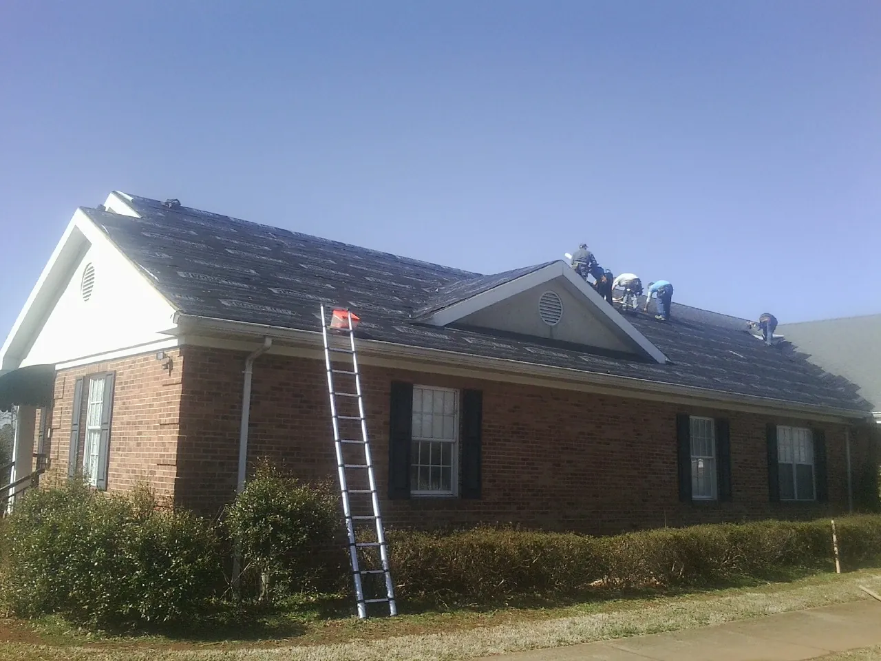 Crew tearing shingles off a brick ranch roof with a ladder set — Emergency Roof Repair work by our crew in Flowood
