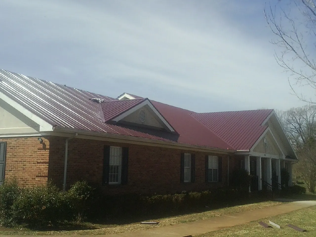 Red metal roof with gabled entries on a long brick building, from a Hail Damage Roof Repair job in Flowood