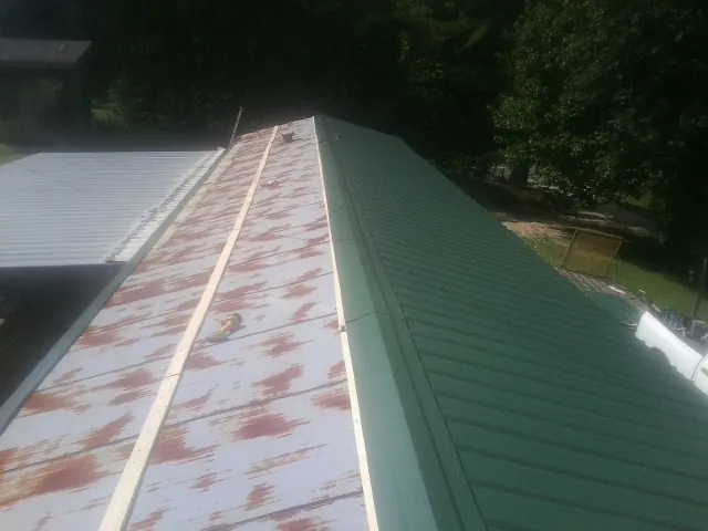 Old rusted panels beside newly installed green metal roofing — Wind Damage Roof Repair by Roofing Brothers in Flowood