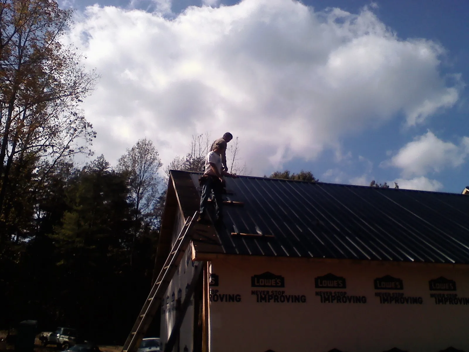 Roofer fastening dark metal panels high against a cloudy sky, from a Roof Inspection job in Flowood