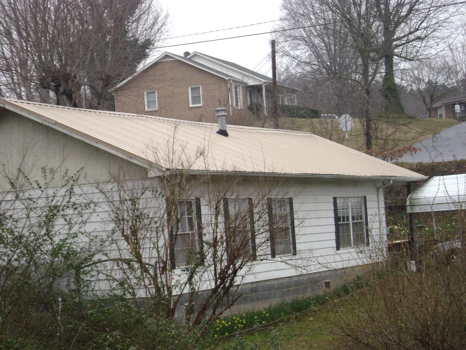 Tan metal roof on a white sided house set into a hillside — Commercial Roofing by Roofing Brothers in Flowood